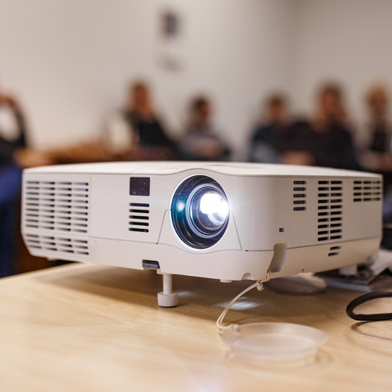 A white projector on a table, pointed towards a wall
