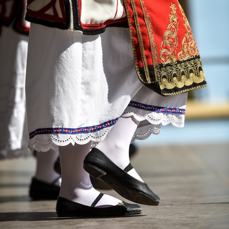 Traditional cultural dance costume with embroidered details and black ballet-style shoes worn by dancers, highlighting the intricate patterns and heritage attire