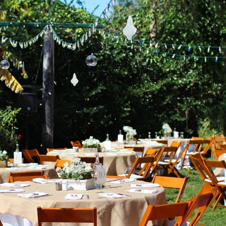 An outdoor wedding reception with tables set for guests, decorated with flowers and lanterns
