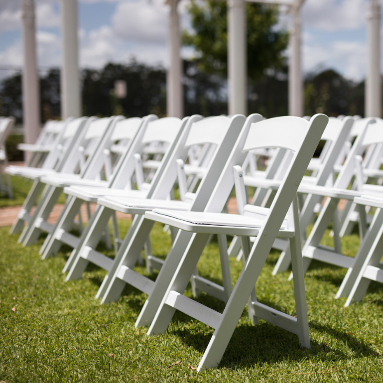 A row of white folding chairs set up on a grassy lawn, ready for an outdoor event