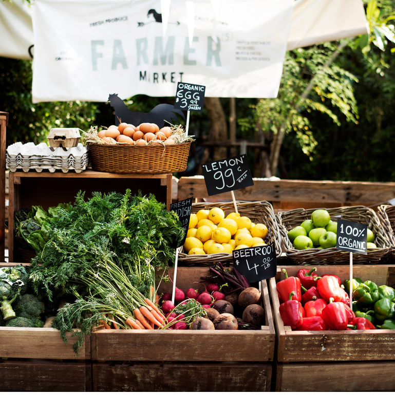 A market stall displaying fresh produce, including eggs, lemons, carrots, beetroot, apples, and peppers