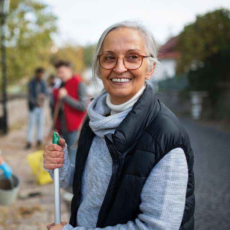 Smiling elderly woman holding a gardening tool during a community outdoor activity