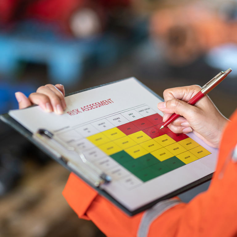 A person in an orange safety vest conducting a risk assessment, filling out a clipboard with a red pen